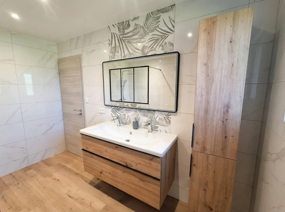 Un ouvrier en combinaison et casque de sécurité blanc mesure une porte intérieure blanche avec un mètre ruban jaune dans un appartement moderne aux murs gris